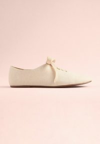 Chaussure plate beige avec un bout pointu, en matériau lin texturé, à lacets à l'avant, et un nœud décoratif sur le dessus. Semelle lisse.