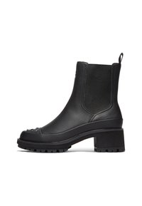 Bota de cuero negra hasta el tobillo con un tacón grueso, paneles elásticos a los lados y tachuelas decorativas en la punta. Suela resistente para tracción.