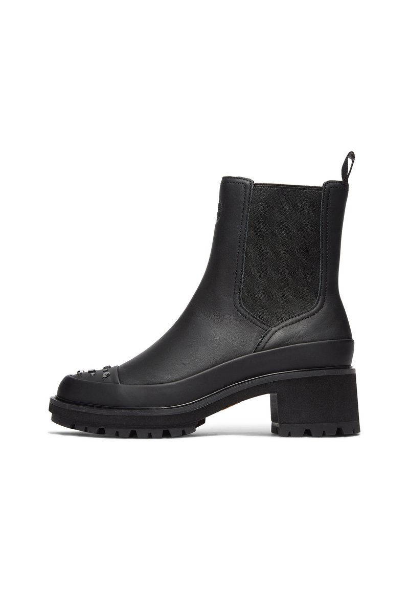 Bota de cuero negra hasta el tobillo con un tacón grueso, paneles elásticos a los lados y tachuelas decorativas en la punta. Suela resistente para tracción.