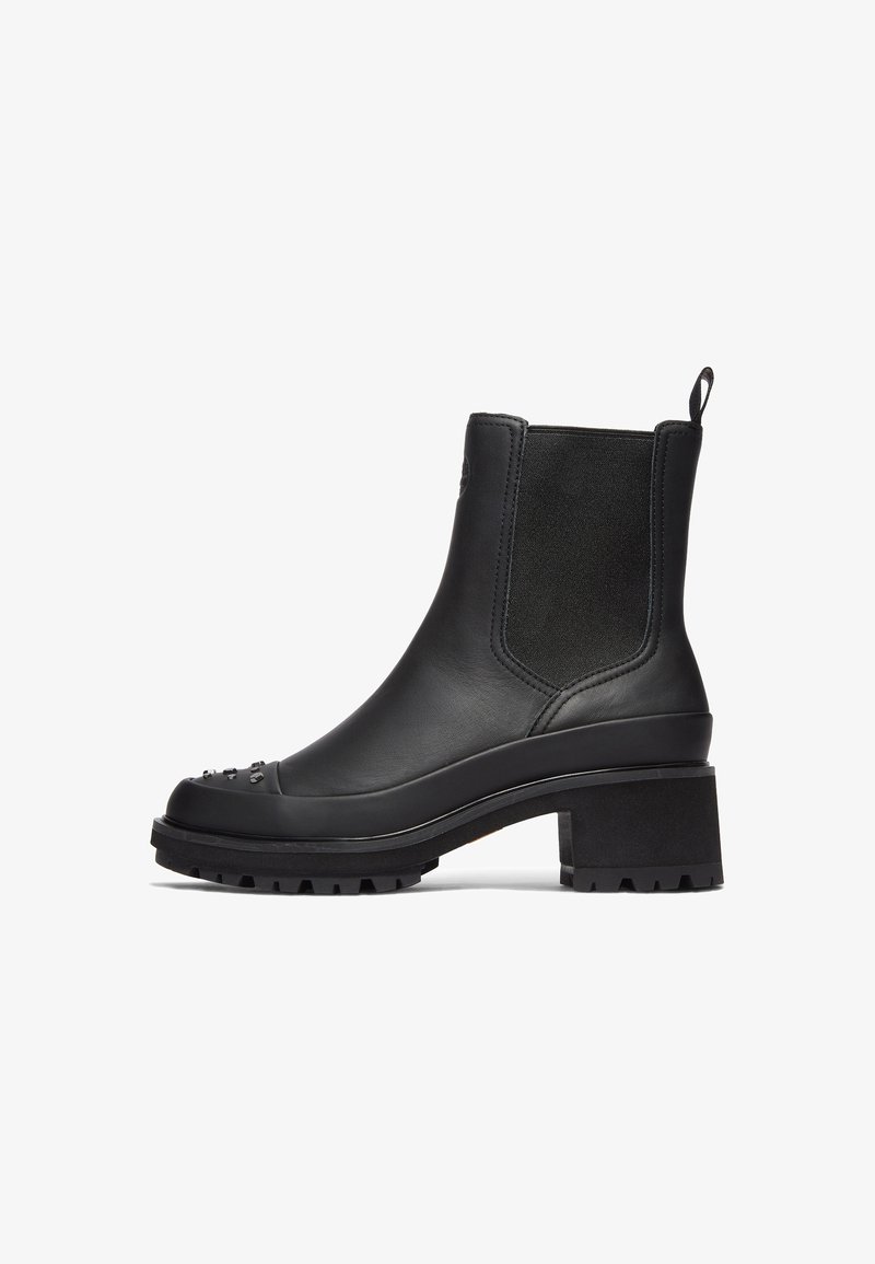 Bota de cuero negra hasta el tobillo con un tacón grueso, paneles elásticos a los lados y tachuelas decorativas en la punta. Suela resistente para tracción.
