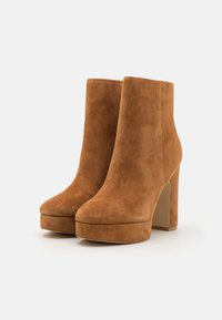 Stivali ankle in suede marrone con punta arrotondata e tacco a blocco alto. Presentano una texture liscia e una suola a piattaforma per un'altezza aggiuntiva.