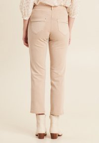 Beige hoge taille broek met een recht model, zakken en zichtbare stikdetails, gecombineerd met lichtbeige enkellaarsjes.