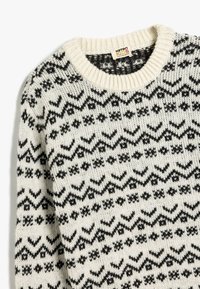 Sweter dziergany w kremowym kolorze z czarnym geometrycznym wzorem, z okrągłym dekoltem i ściągaczami na rękawach. Wykonany z miękkiego materiału z wełny.