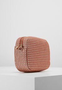 Borsa cosmetica marrone con texture e motivo geometrico, dotata di una zip dorata e di forma rettangolare, posata su un piedistallo bianco.