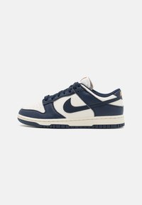 Navy and cream leather sneaker with perforated toe, rounded shape, textured accents, Nike logo, and contrasting sole.