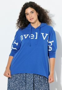 Felpa con cappuccio blu dal taglio ampio con scritta bianca "Travel Vibe" sul davanti e sulla manica. Presenta un cappuccio con coulisse e maniche lunghe.