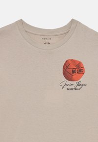 Ljust beige bomull t-shirt med en tryckt röd basketboll med texten "NO LIMITS" och "Junior League BASKETBALL" i svart. Rund halsringning.