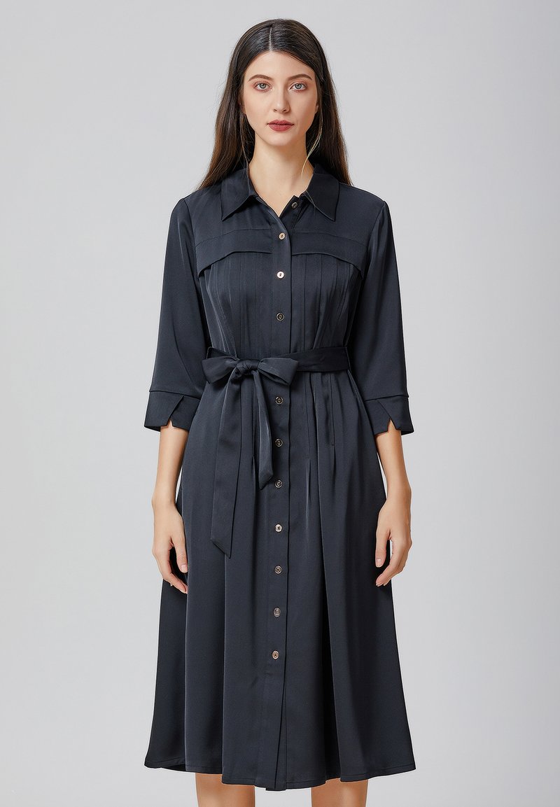 Robe noire à boutons, confectionnée dans un tissu lisse. Présente un corsage ajusté, une jupe fluide et une ceinture à nouer à la taille. Design de col classique.