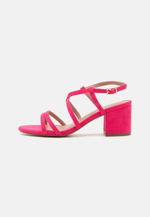 Sandale à talon en daim rose avec bout ouvert, dotée de multiples lanières croisées et d'un talon bloc pour la stabilité. Fermeture à boucle sur la bride de cheville.