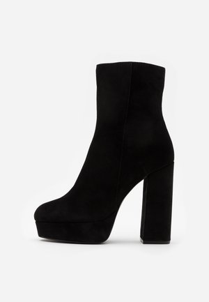 Bottine en daim noir avec un talon haut et épais ainsi qu'une semelle plateforme, vue de profil sur un fond clair uni.