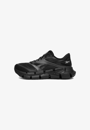 Zapato deportivo negro con parte superior de malla y suela de goma texturizada. Cuenta con cierre de cordones, talón reforzado y un diseño curvado para mayor comodidad.