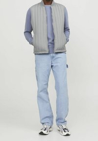 Grå, vadderad väst med hög krage, över en ljusblå sweatshirt. Bärs med ljusblå jeans och klumpiga vita sneakers.