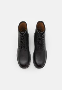 Stivaletti neri in pelle con parte superiore testurizzata, lacci e rivestimento interno marrone. Suola in gomma resistente con design della punta arrotondata.