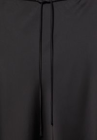 Tissu noir avec une paire de fines cordons pendants centrés verticalement sur un fond uni.
