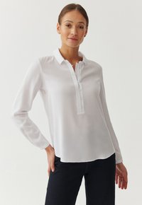 White long-sleeve blouse with a pointed collar, button placket, and smooth texture, featuring a relaxed fit and curved hem.