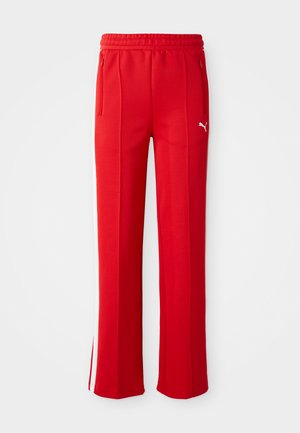 Røde joggebukser laget av et glatt stoff, med snøring i midjen, sidelommer med glidelås og hvite sidestriper. Logo på øvre del av låret.