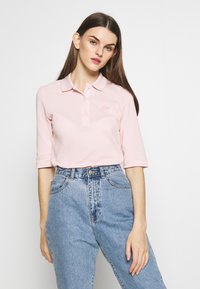 Polo shirt rosa chiaro con tre bottoni, colletto a coste e maniche lunghe fino al gomito, abbinato a jeans in denim blu a vita alta.
