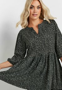 Abito nero con arricciatura in vita, caratterizzato da un motivo a pois bianchi, colletto e maniche a tre quarti.