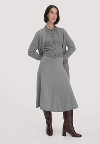 Grauer Strickcardigan über einem passenden knöpfbaren Oberteil und einem langen Rock. Verfügt über eine strukturierte Oberfläche und burgunderfarbene Stiefel bis zum Knie.