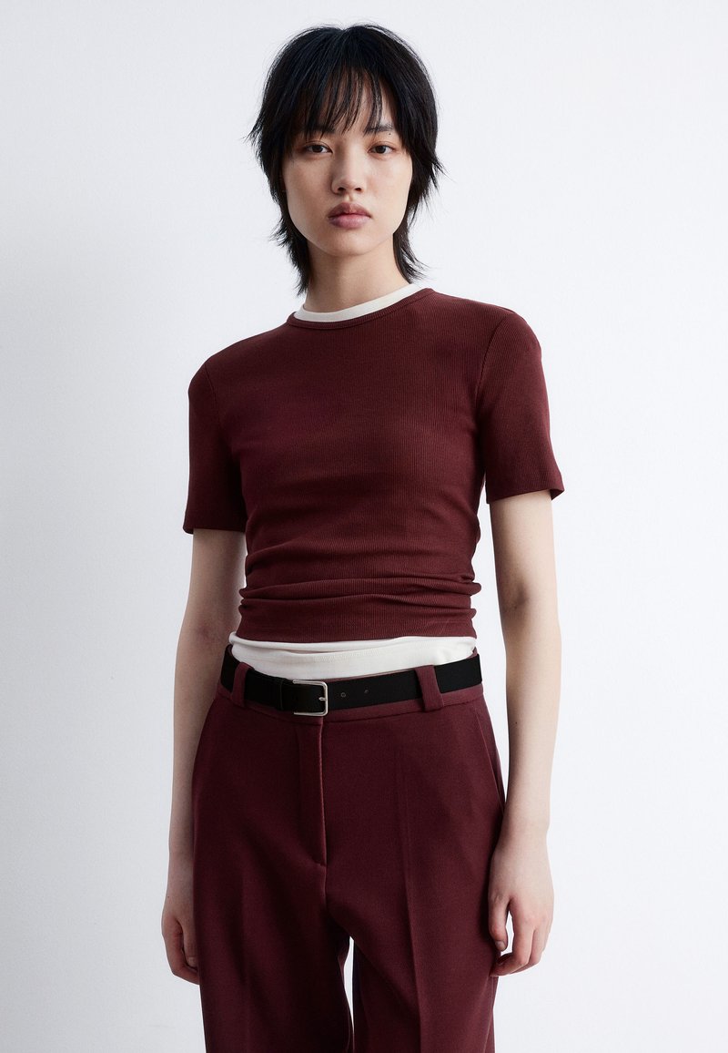 Burgundy ribbed t-shirt with short sleeves and contrasting white neckline, paired with dark trousers and a black belt, featuring a smooth texture.