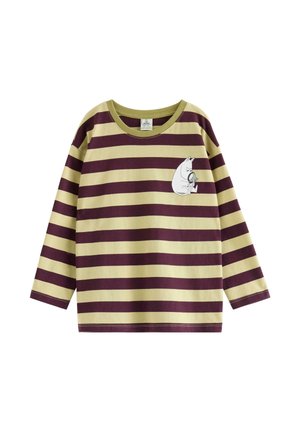 Ung dreng smilende, iført en beige og vinrød stribet langærmet trøje, blå hue, mørkeblå jeans og beige sko.