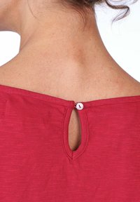 Red top featuring a scoop neckline, a small keyhole opening at the back, and a button closure. Fabric appears textured with subtle patterns.