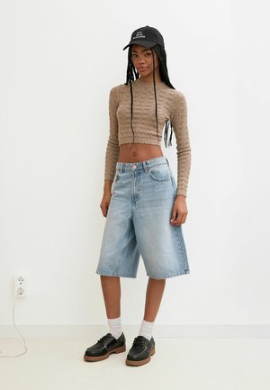 Bruine gebreide crop top, lichtblauwe denim Bermuda shorts, zwarte schoenen met dikke zolen, witte sokken, zwarte pet met tekst.