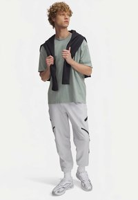 Gaiši zaļa pārliela izmēra T-krekls, melns džemperis pārmests pār pleciem, balti sporta bikses ar melniem akcentiem un sudraba krāsas sporta apavi. Cirtaini mati.