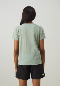 Tricou scurt cu mânecă în nuanța verde mentă, cu un guler rotund și textură netedă. Este asortat cu pantaloni scurți negri ce au un detaliu subtil de etichetă.