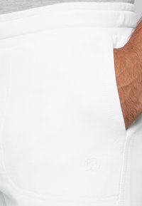 Joggers blancos de algodón con una textura suave, cintura elástica y un pequeño logo bordado en el bolsillo.