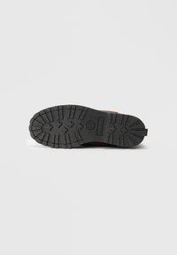 Suela de una bota marrón de Timberland que muestra profundas bandas de rodadura y el logo de la marca sobre un fondo blanco limpio.