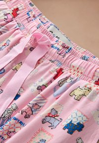 Pantalon à taille élastique rose avec lien en tissu et motif imprimé de petits chiens colorés variés et formes décoratives.
