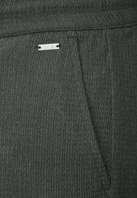 Mörkgrå texturerade tygbyxor med ett subtilt ribbat mönster och en metallisk logotagg märkt "CECIL" nära midjan.