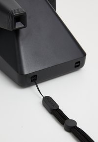 Black accessory with a textured grip and a cord. Features a small logo tag and a smooth, angled base, designed for functionality.