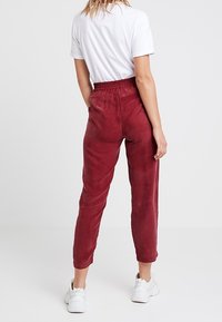 Pantalons rouges texturés avec une coupe décontractée, une taille élastique et des jambes fuselées, associés à des baskets blanches et une chemise à manches courtes.