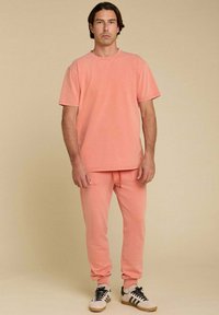 T-shirt en coton pêche et joggers assortis avec une taille élastique, des poignets ajustés et une coupe décontractée. Chaussures noires et blanches.