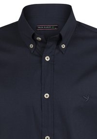 Camisa de botones azul marino hecha de tela suave. Presenta un cuello clásico, botones blancos y un pequeño logo bordado en el pecho.