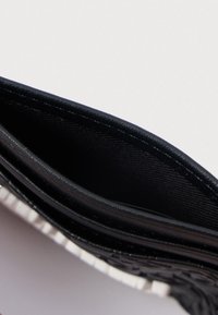 Carteira de couro preta vazia vista de cima contra um fundo claro e liso.