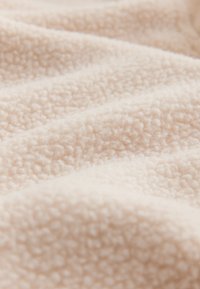 Tessuto in pile beige con una superficie morbida e strutturata, caratterizzato da un motivo leggermente rialzato e pieghe delicate.