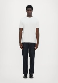 Hvit kortermet t-skjorte, mørk denim jeans og svarte sko. T-skjorten har en lomme; jeansene har rett skjæring og subtil søm.