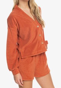 Pomarańczowa bluza z polaru na guziki z dekoltem w serek, długimi rękawami i luźnym krojem, w zestawie z dopasowanymi szortami z polaru, oba elementy o miękkiej strukturze.