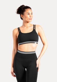 Sujetador deportivo negro con dos tirantes finos y una banda a rayas. Combinado con mallas negras de talle alto que tienen una cinturilla a rayas a juego.