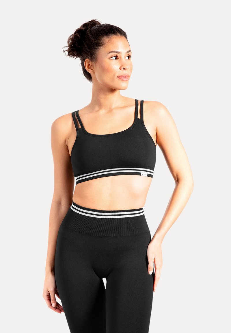 Sujetador deportivo negro con dos tirantes finos y una banda a rayas. Combinado con mallas negras de talle alto que tienen una cinturilla a rayas a juego.