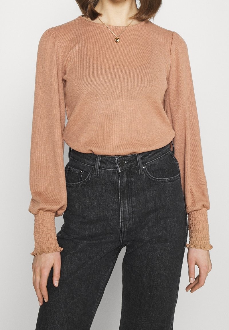 Haut à manches longues côtelé couleur pêche avec poignets élastiqués et volantés, associé à un jean en denim noir taille haute. Encolure ronde simple.