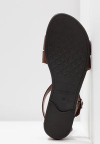Base en cuir marron de sandale avec une semelle en caoutchouc noir texturée. Comprend une bride latérale et un détail de boucle, taille marquée 37.