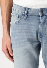 Jeans en denim bleu clair avec une coupe droite, design à cinq poches et fermeture à bouton supérieur. Le tissu a une texture douce et légèrement usée.