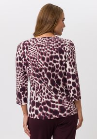 Bordeauxrotes und cremefarbenes Oberteil mit einem gepunkteten Muster, Dreiviertelärmel und rundem Ausschnitt. Glatte Stoffqualität mit einem leichten Glanz.