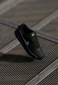 Nike sneakers neri con una finitura testurizzata, caratterizzati da uno swoosh grigio, lacci e una suola ammortizzata. Accentuati da un logo bianco.