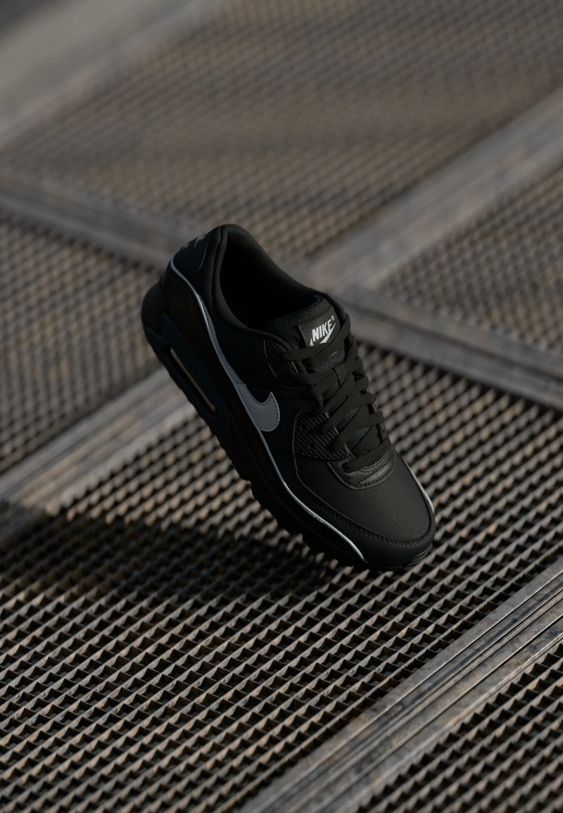 Nike sneakers neri con una finitura testurizzata, caratterizzati da uno swoosh grigio, lacci e una suola ammortizzata. Accentuati da un logo bianco.
