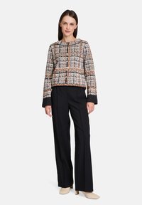 Woman wearing a patterned, textured, cropped sweater with shades of cream, black, and brown, paired with black wide-leg trousers and beige shoes.
